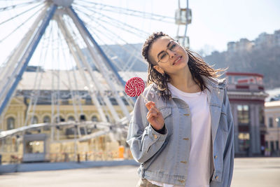 Portrait of hipster woman standing against ferris wheel in city