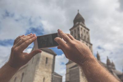 Cropped image of hand holding smart phone against sky