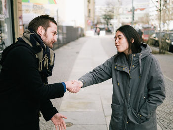 Friends shaking hands on sidewalk in city