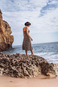 Side view of woman standing on rock at beach against sky