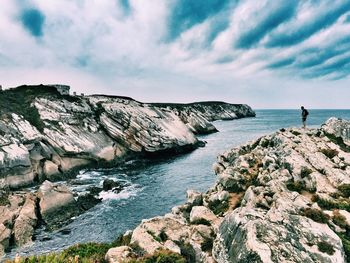 Scenic view of rocks next to sea against cloudy sky