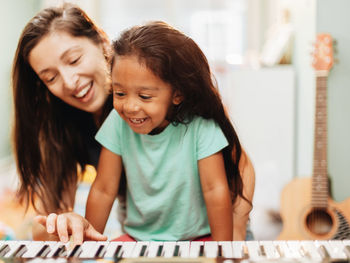 Happy mother teaching piano to daughter at home