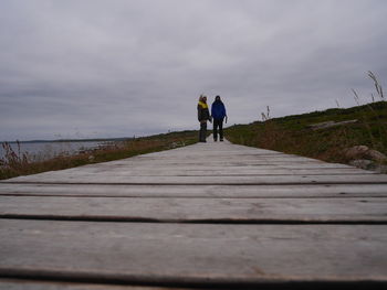 Surface level shot of people standing on boardwalk against cloudy sky