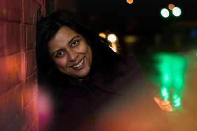 Portrait of smiling mature woman leaning on brick wall at night