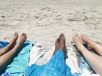 Low section of women lying on textiles at beach during sunny day