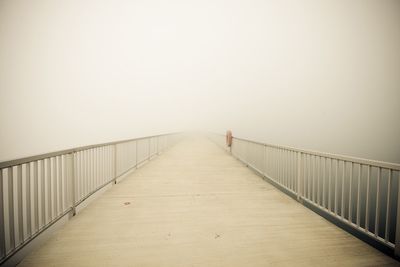 Empty footbridge in fog against sky