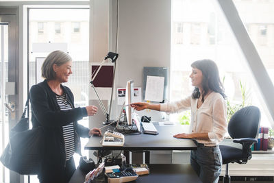 Businesswoman giving card to female entrepreneur at counter in office