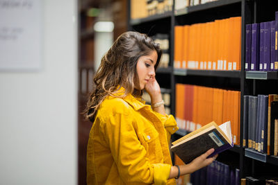 Side view of young woman reading book at library