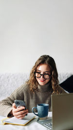 Young woman using mobile phone while sitting on table against white background