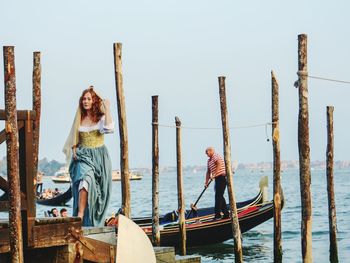 Women standing on wooden post by sea against sky