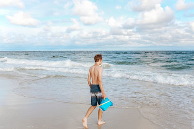 Full length of teenage boy on beach against sky