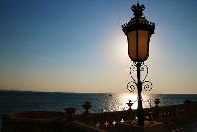 Street light by sea against sky during sunset