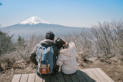 Rear view of woman leaning on man while sitting on observation point against clear sky