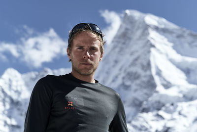 Low angle portrait of young man standing against snowcapped mountains