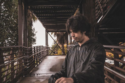 Young man looking down while standing on bridge