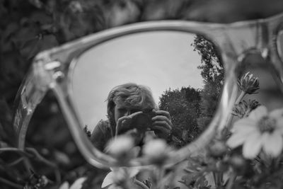 Reflection of woman photographing through camera in sunglasses on grass