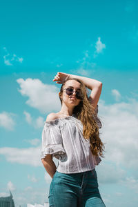 Low angle view of young woman standing against blue sky