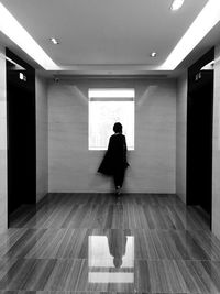 Rear view full length of woman standing against window in building passage