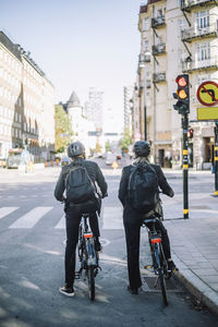 Rear view of business colleagues with bicycles waiting at traffic signal