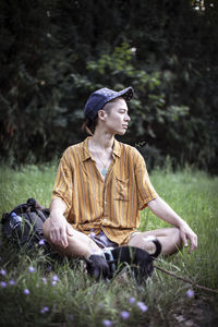 Handsome mixed race person in baseball cap sits in green summer grass