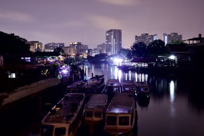Illuminated buildings by river against sky in city at night
