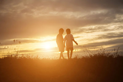 Silhouette friends standing on field against sky during sunset