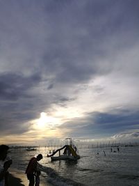 Silhouette people on sea against sky during sunset