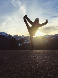 Man with arms outstretched against sky during sunset