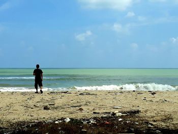 Rear view of man standing on beach against sky