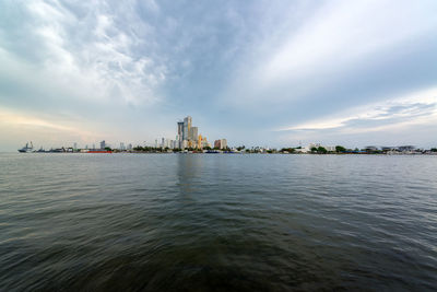 Sea by city against cloudy sky