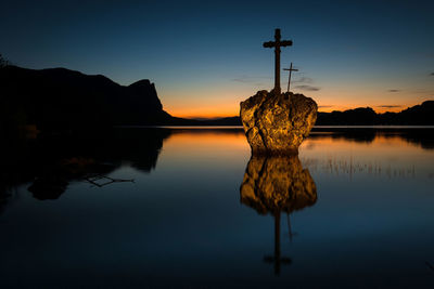 Close-up of cross on rock in lake against sky during sunset