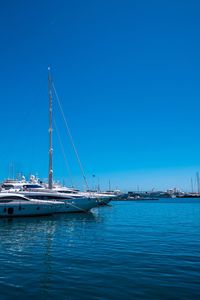 Sailboats moored in sea against clear blue sky