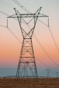 Low angle view of electricity pylon against sky during sunset