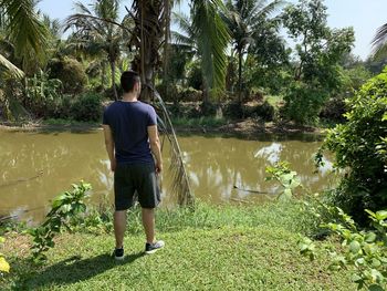 Rear view of man standing by lake against trees