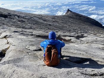 Rear view of woman sitting on rock against sky