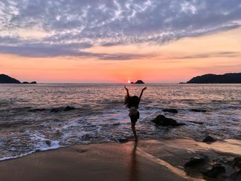 Silhouette woman standing on beach against sky during sunset