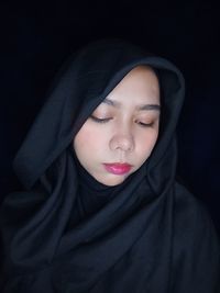 Portrait of beautiful young woman wearing hijab against black background