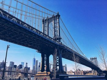 Low angle view of manhattan bridge in city against clear blue sky