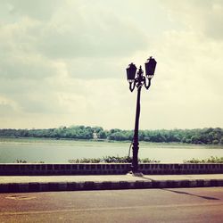 Street lamp by river against cloudy sky