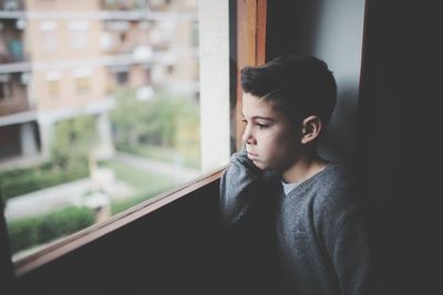 Close-up of boy looking through window at home