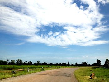 Dirt road amidst field against sky