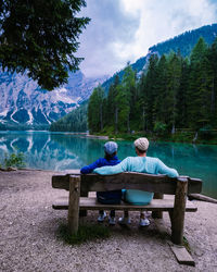 People sitting on bench by lake against mountains