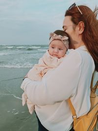 Side view of mother and baby standing at beach