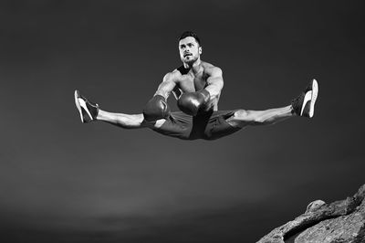 Full length of shirtless young man climbing outdoors