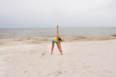 Full length of mid adult woman exercising at beach against clear sky