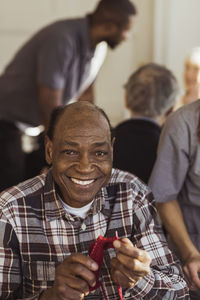 Portrait of smiling elderly man knitting at retirement home