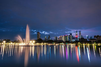 Illuminated city by river against sky at night