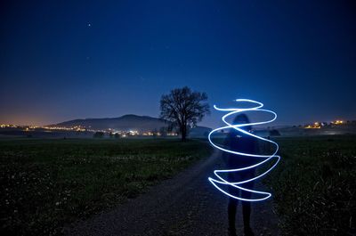 Person with light painting on road against sky at night