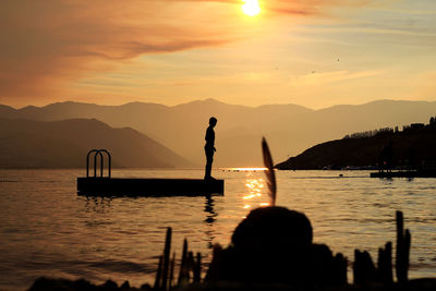 Silhouette boy standing on floating platform amidst lake