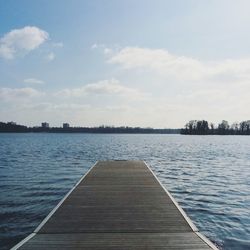 Jetty leading to calm sea against cloudy sky